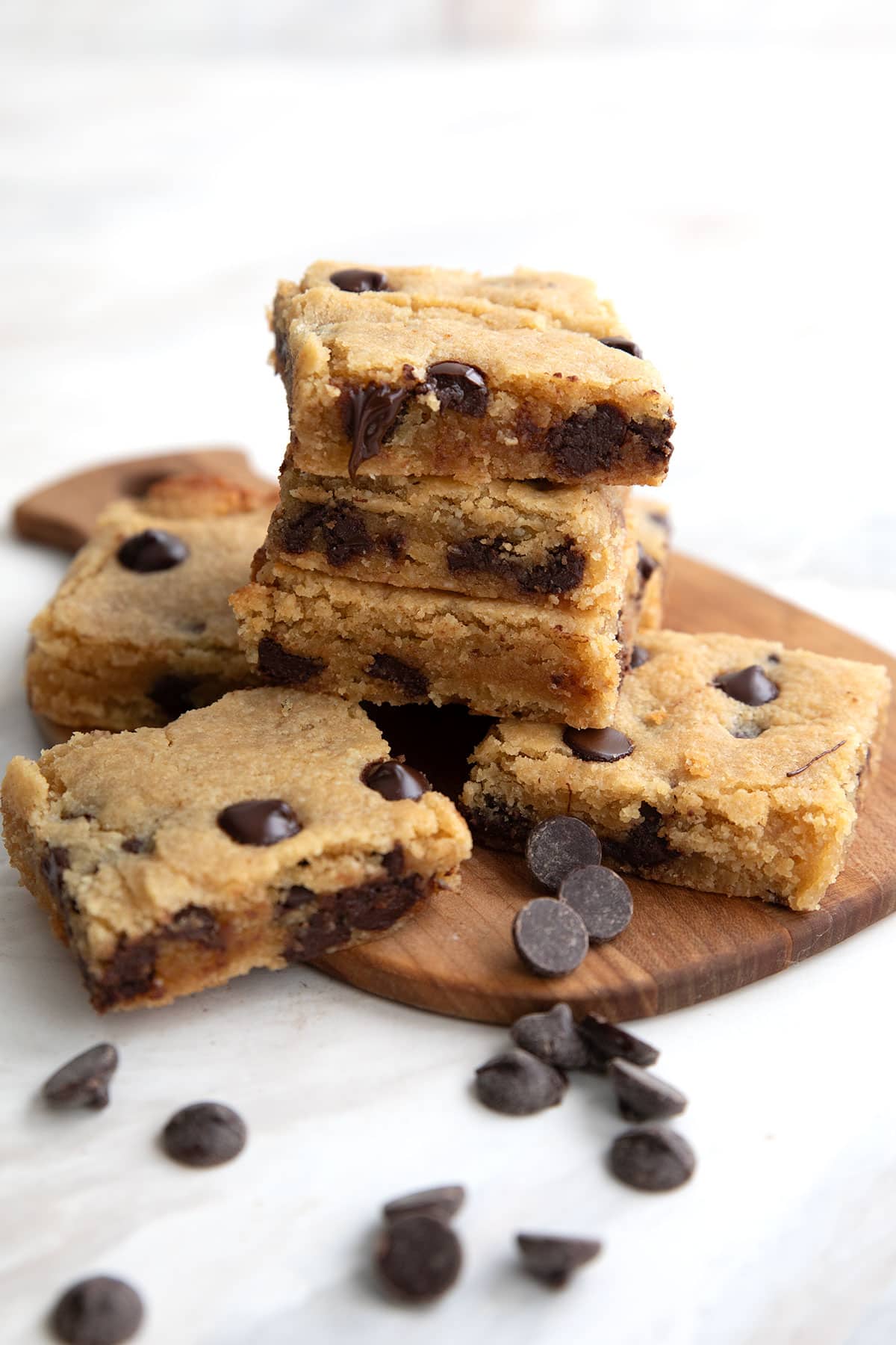 A stack of Brown Butter Keto Blondies on a wooden cutting board with chocolate chips strewn around.