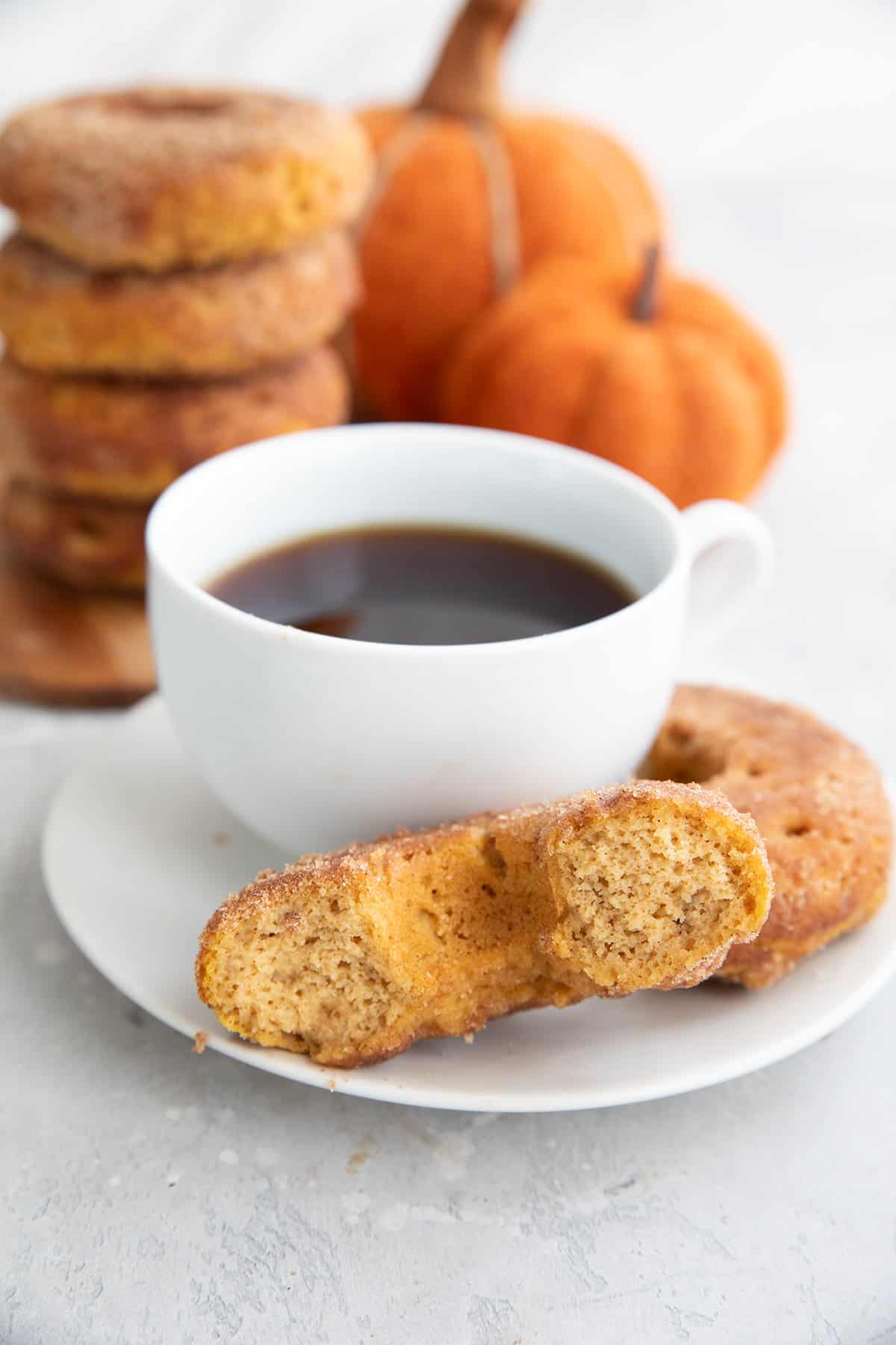 A Keto Pumpkin Spice Donut broken open on a plate with a cup of coffee.