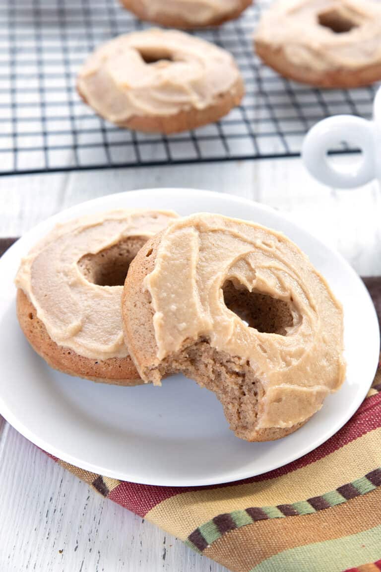 Two keto donuts on a white plate with a bite taken out of the top one.