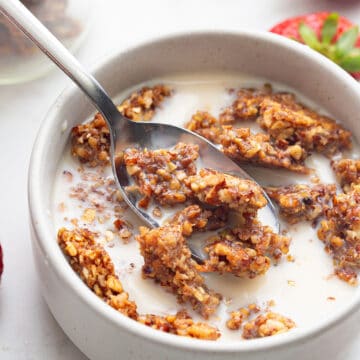 Crunchy keto granola in a white bowl with milk, with a spoonful being lifted out of it.