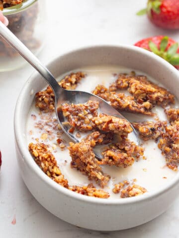 Crunchy keto granola in a white bowl with milk, with a spoonful being lifted out of it.