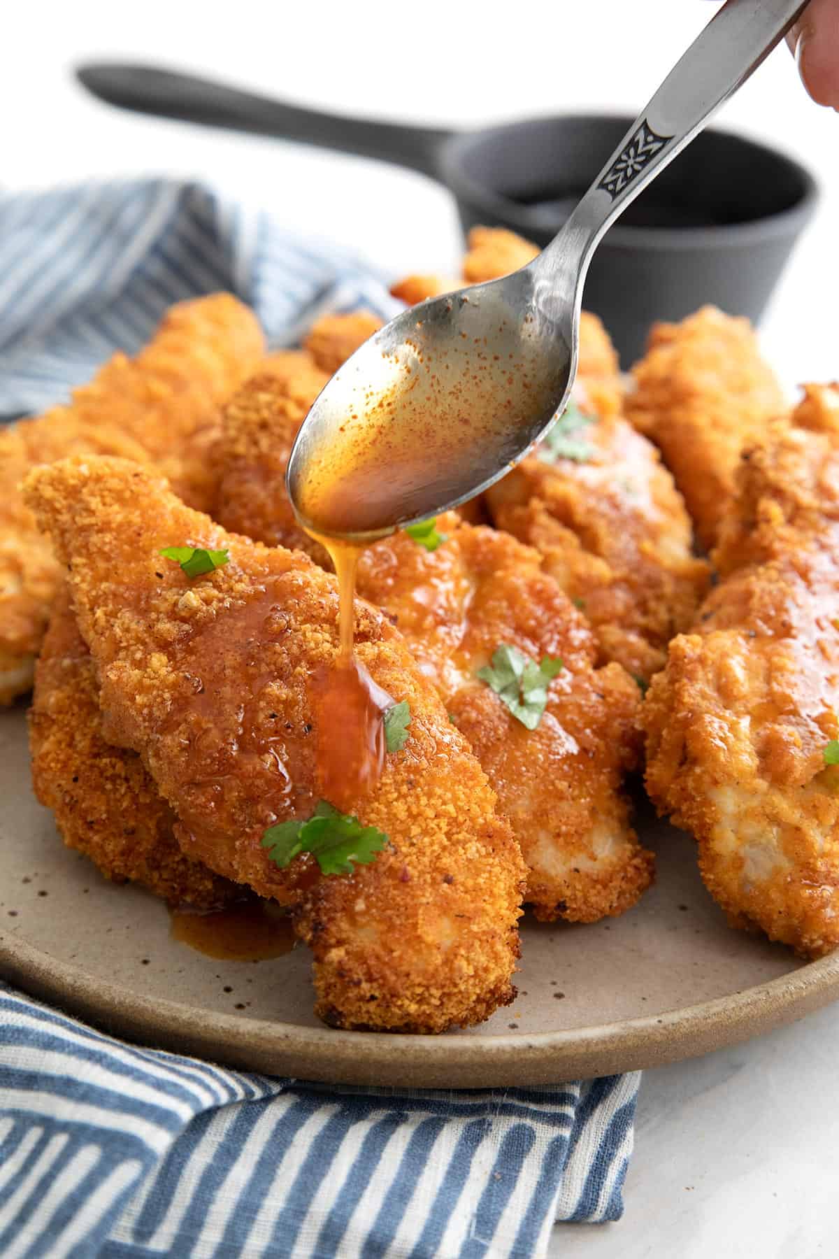 A spoon drizzling glaze over air fried keto chicken tenders on a plate.