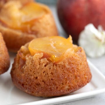 Keto Peach Upside Down Cakes on a white platter with a peach in the background.