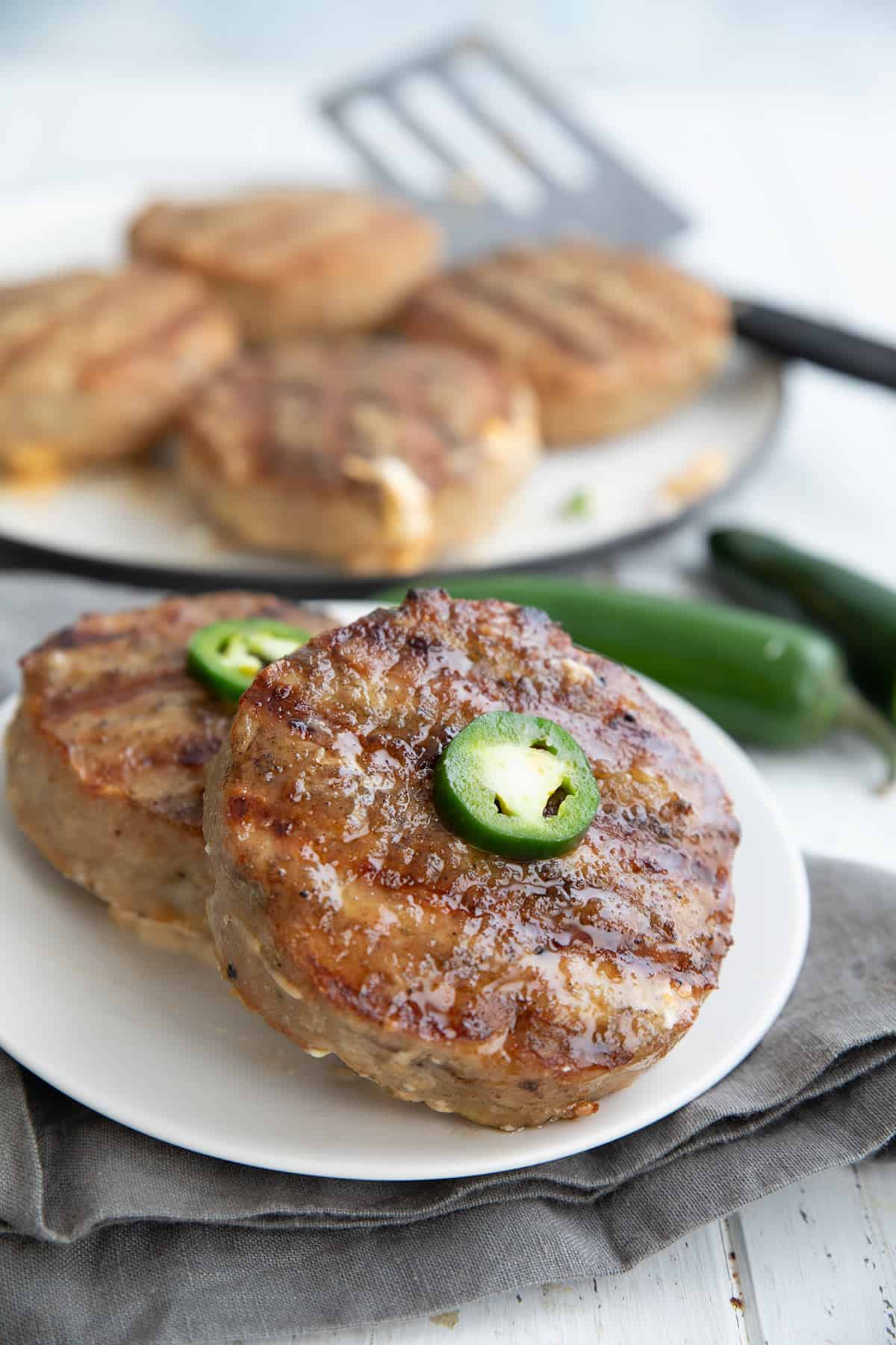 Two keto turkey burgers on a white plate with sliced jalapeño on top.