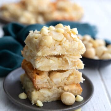 A stack of Keto Coconut Macadamia Bars on a grey plate with macadamia and white chocolate chips strewn around.