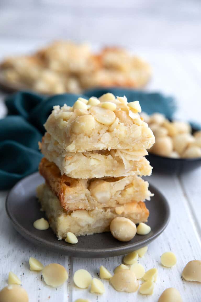 A stack of Keto Coconut Macadamia Bars on a grey plate with macadamia and white chocolate chips strewn around.