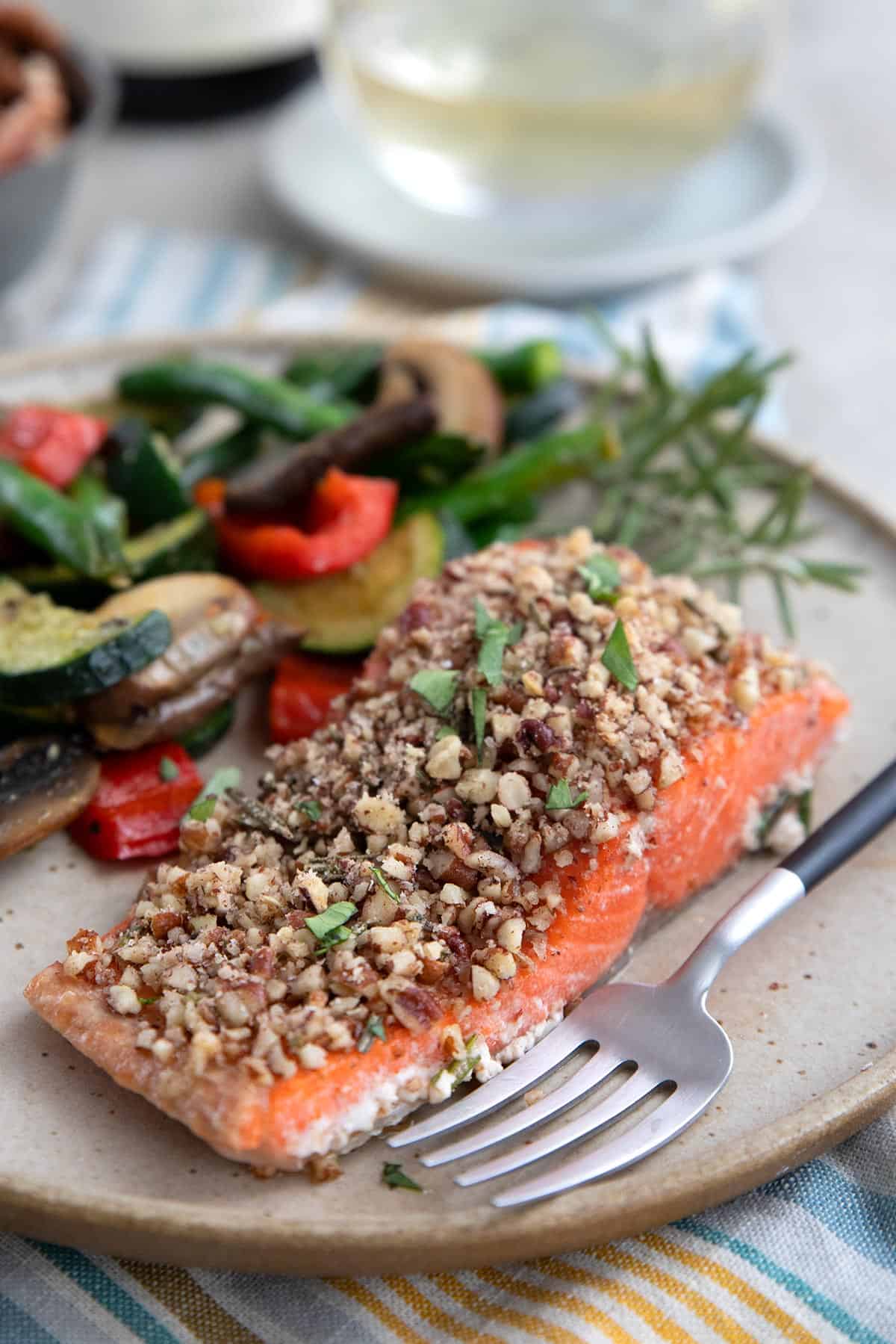 A serving of Pecan Crusted Salmon on a plate with sautéed veggies.