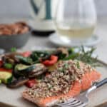 A piece of Pecan Crusted salmon on a rustic plate with a glass of wine in the background.