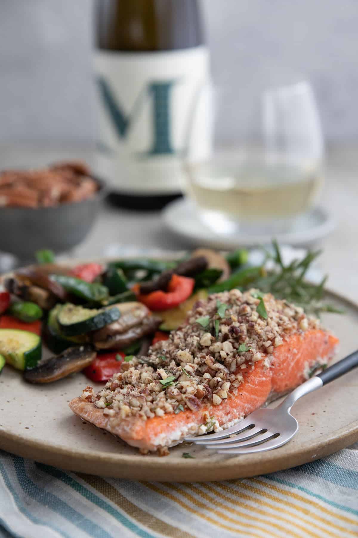 A piece of Pecan Crusted salmon on a rustic plate with a glass of wine in the background.