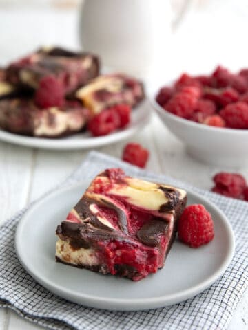 A Keto Raspberry Cheesecake Brownie on a grey plate in front of a bowl of fresh raspberries.