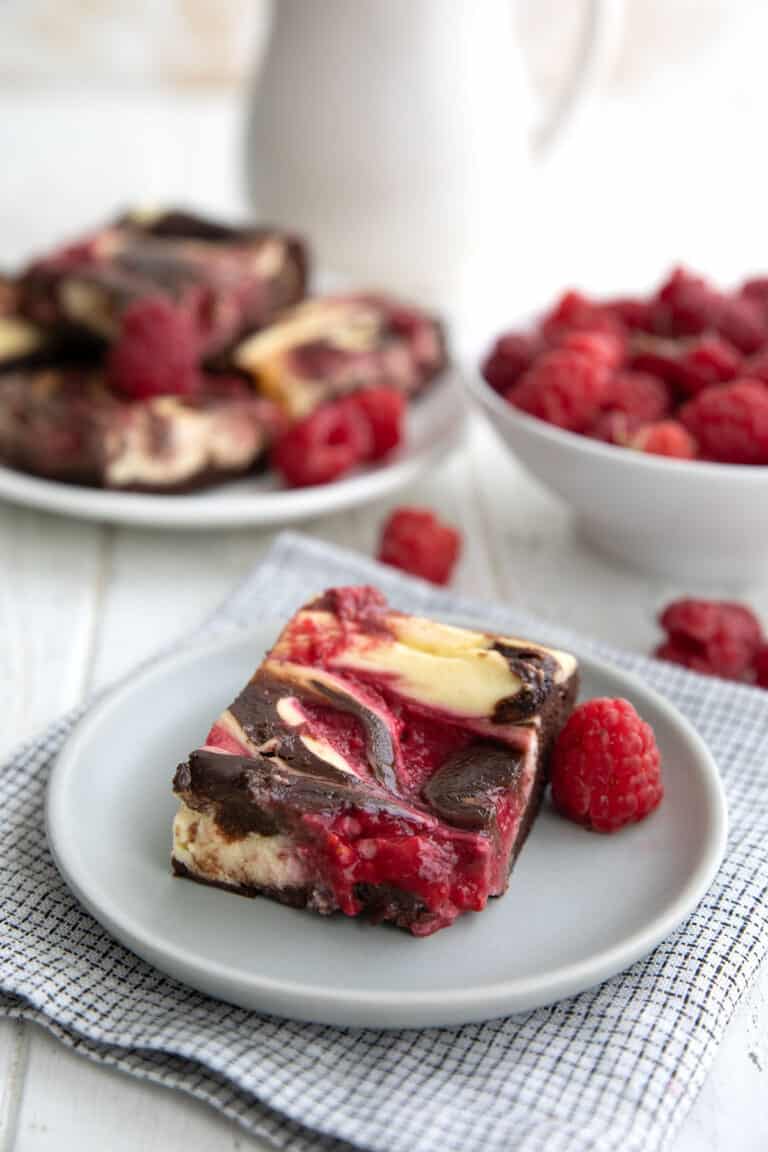 A Keto Raspberry Cheesecake Brownie on a grey plate in front of a bowl of fresh raspberries.