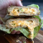 A hand holding up a stuffed turkey burger in a lettuce wrap, with melted cheese oozing out.