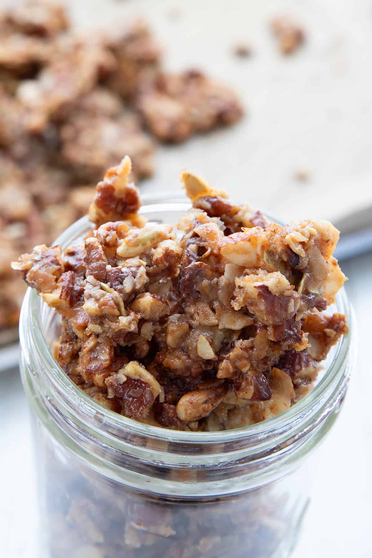 Keto Granola in a glass jar in front of a pan of baked granola.