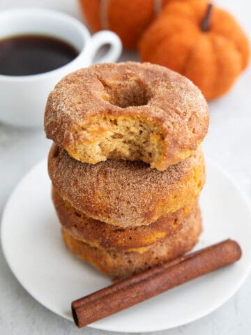 A stack of Keto Pumpkin Donuts on a white plate with a bite taken out of the top one.