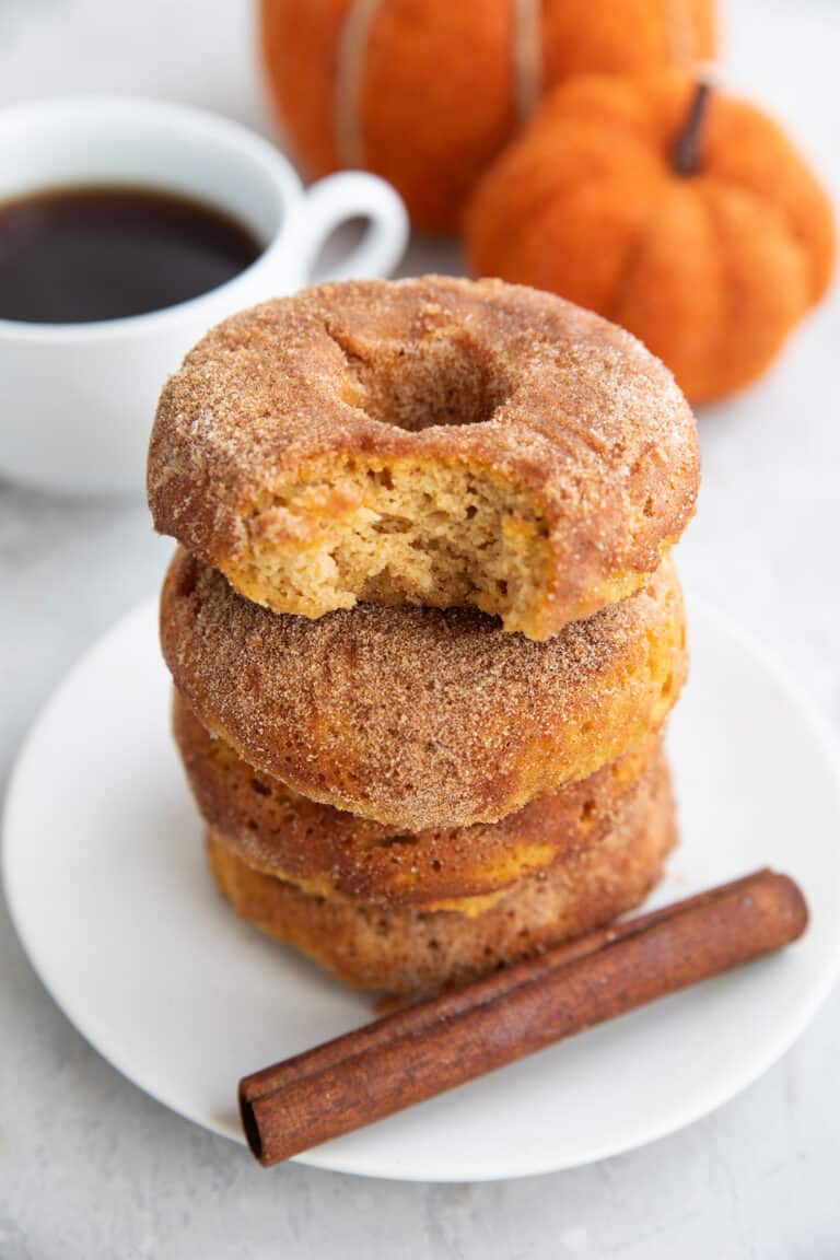 A stack of Keto Pumpkin Donuts on a white plate with a bite taken out of the top one.