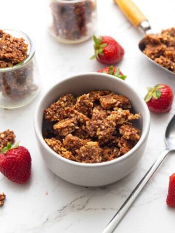 A bowl with keto granola chunks and strawberries with more granola next to it