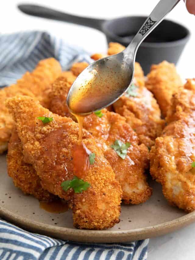A spoon drizzling glaze over air fried keto chicken tenders on a plate.