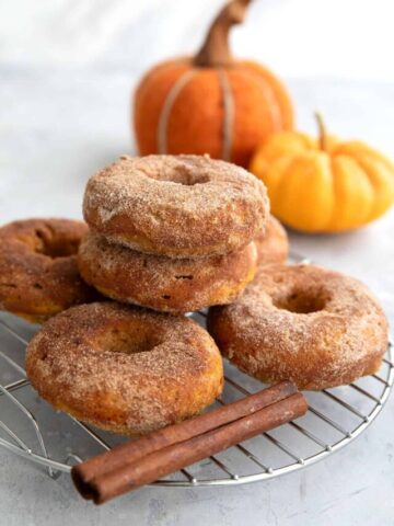 Pumpkin Donuts in a stack on a cooling rack in front of a mini pumpkin.