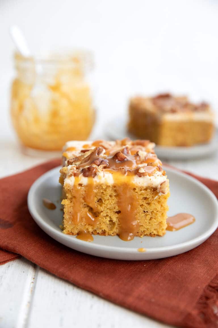 A piece of keto pumpkin poke cake on a gray plate over a dark orange napkin, with a jar of caramel sauce in the background.