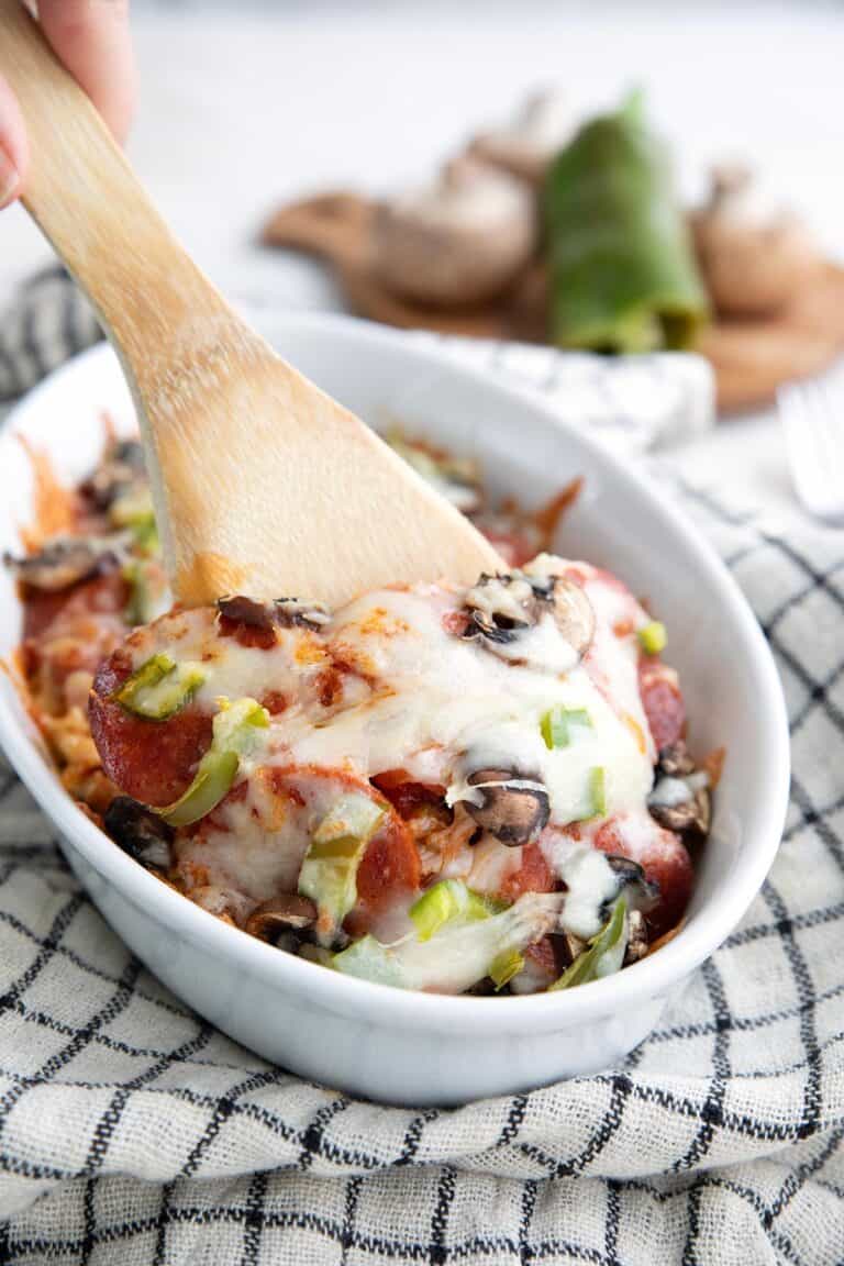 Crustless pizza in a white baking dish with a wooden serving spoon digging into it.