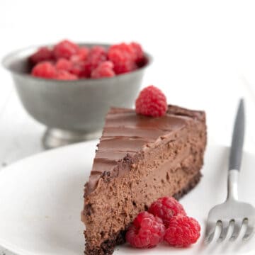 A slice of Keto Chocolate Cheesecake on a white plate with raspberries and a fork.