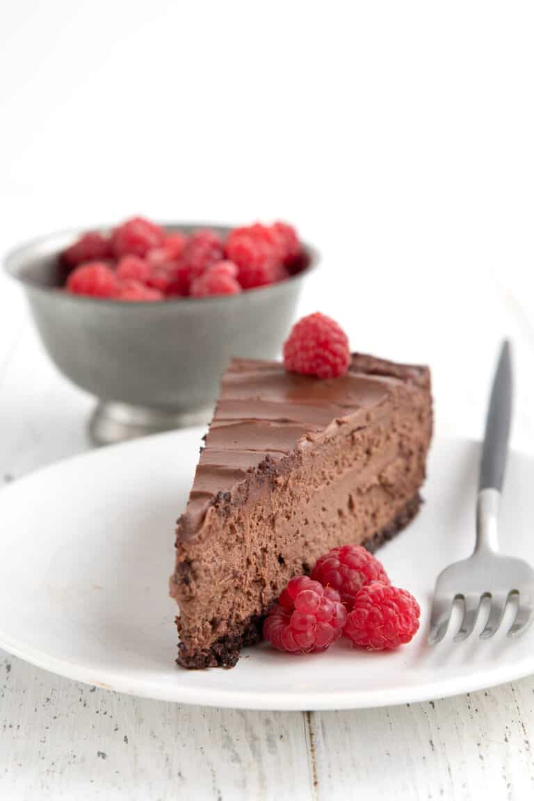 A slice of Keto Chocolate Cheesecake on a white plate with raspberries and a fork.