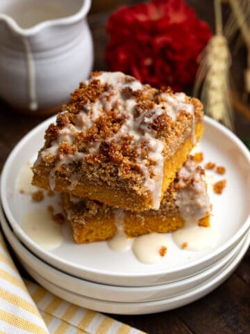 Two Keto Pumpkin Crumb Cake on a stack of white plates with a yellow striped napkin.