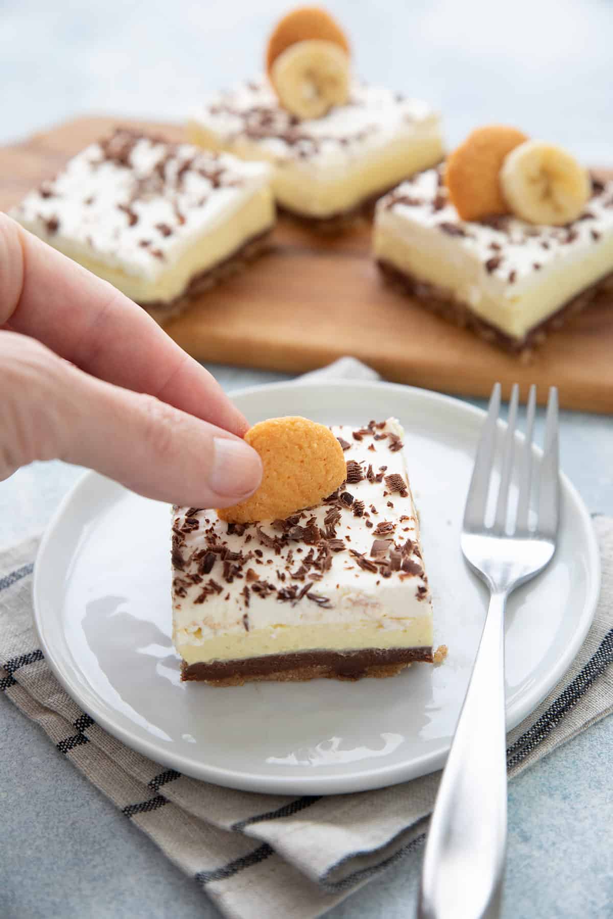 A hand placing a vanilla wafer on top of a Keto Banana Cream Pie Bar.