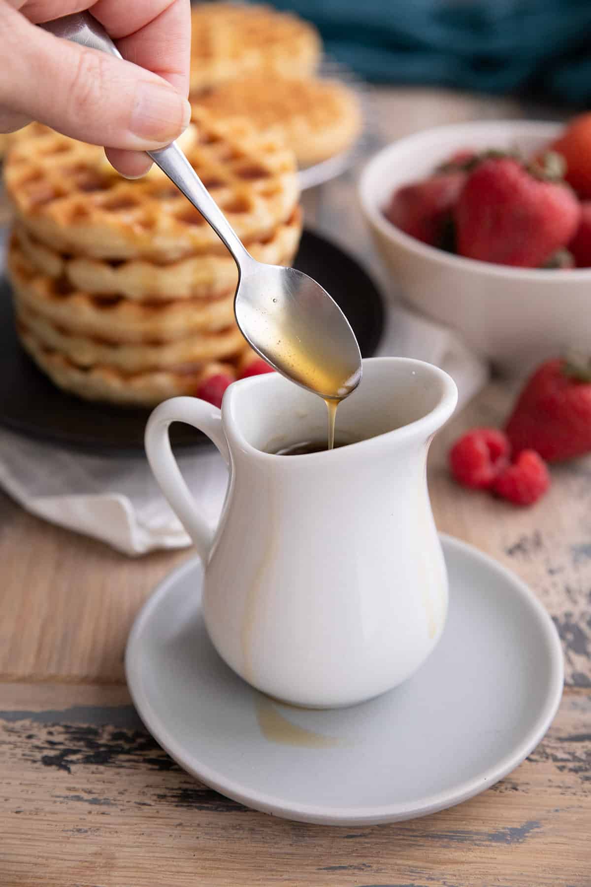 A hand drizzling sugar free pancake syrup into a white pitcher.