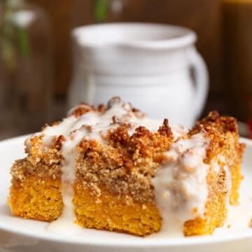 A slice of Keto Pumpkin Crumb Cake on a white plate with a white pitcher in behind.