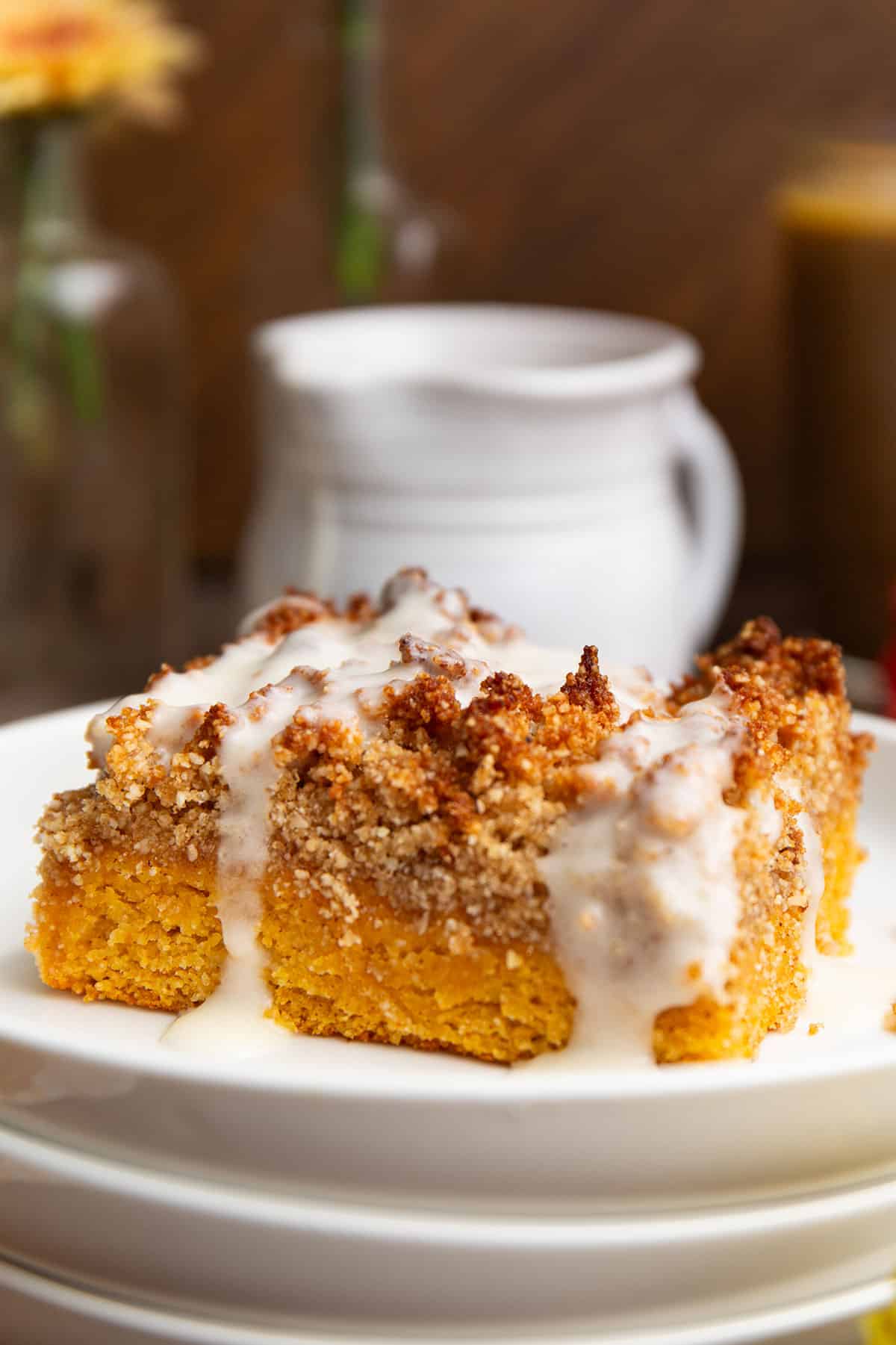 A slice of Keto Pumpkin Crumb Cake on a white plate with a white pitcher in behind.