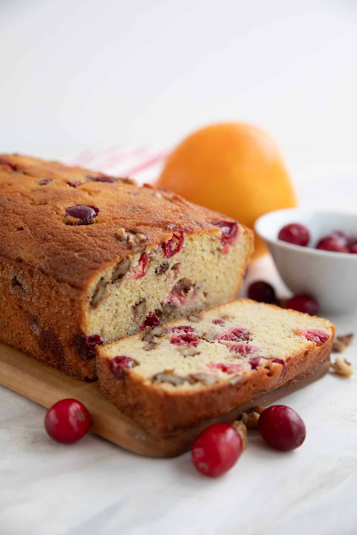 Keto Cranberry Orange Bread on a wooden cutting board with cranberries and walnuts in front.