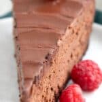 Titled Pinterest image: close up shot of a slice of Keto Chocolate Cheesecake on a white plate with raspberries.