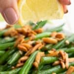 Titled image of a hand squeezing lemon over a plate of Green Beans Almondine.