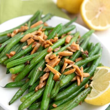 Green Beans Amandine on a white plate with lemons the background.