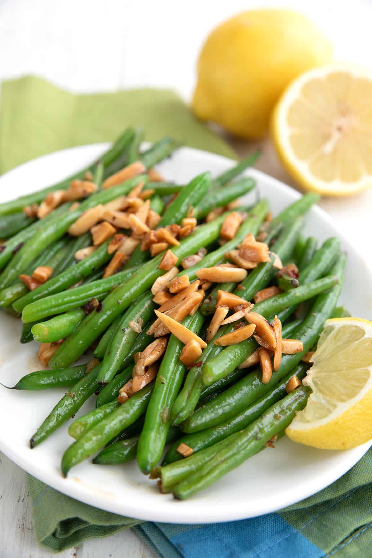 Green Beans Amandine on a white plate with lemons the background.
