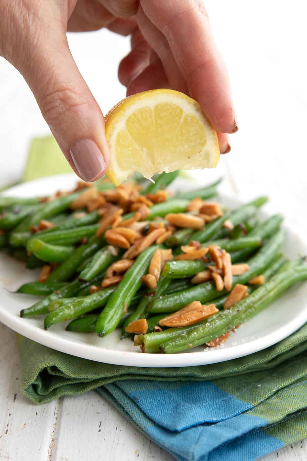 A hand squeezing lemon over Green Beans Amandine.