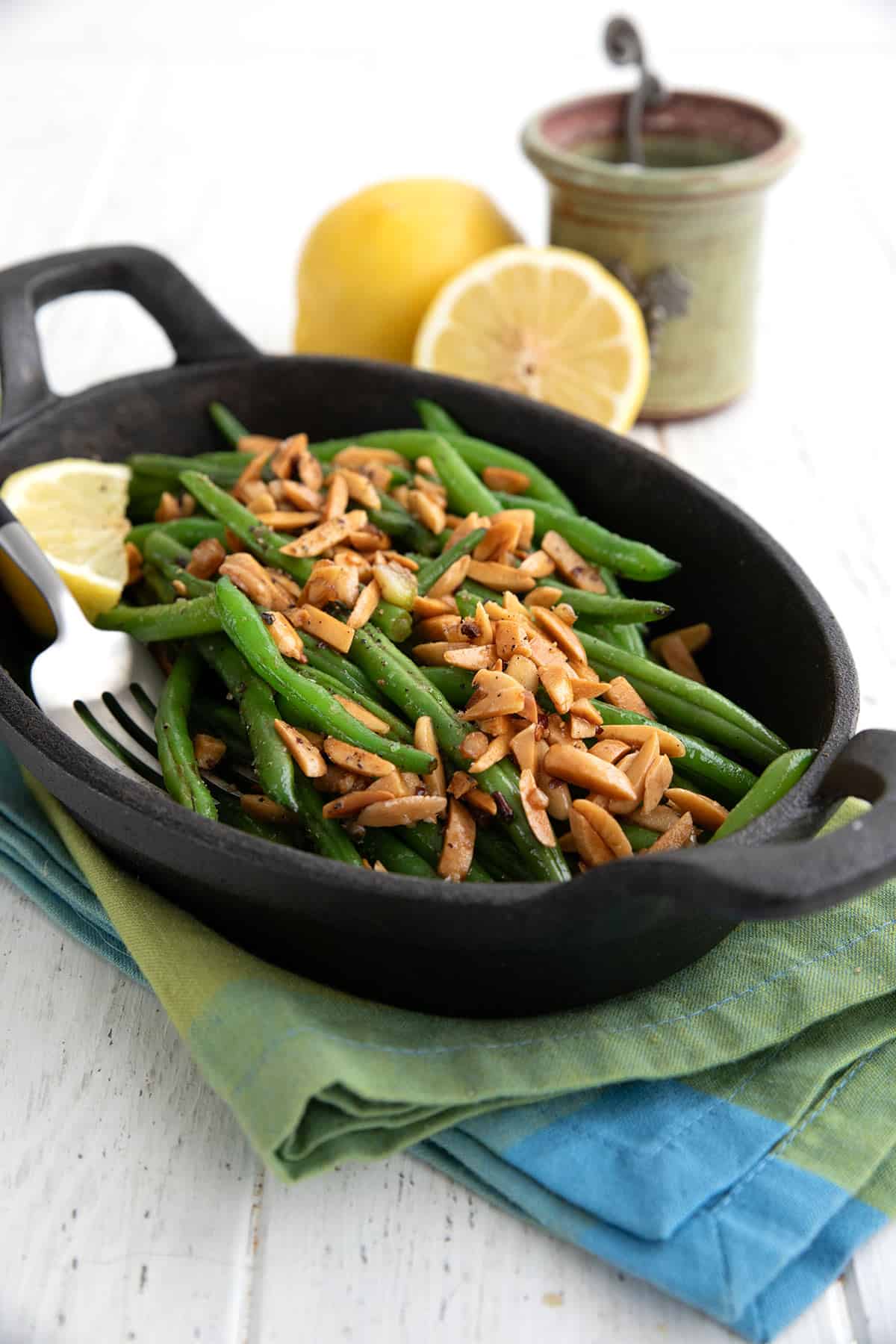 Green Beans Almondine in a black oval dish over a green and blue napkin.