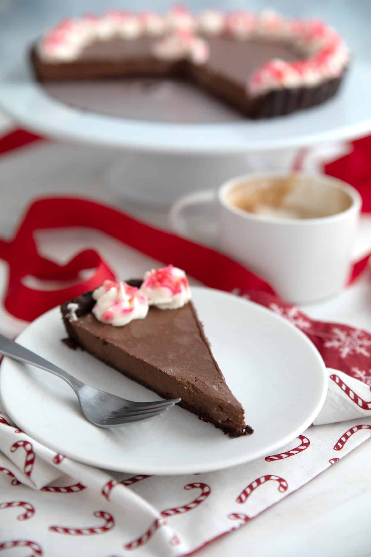 A slice of keto peppermint truffle tart on a white plate over a white napkin with candy canes on it.