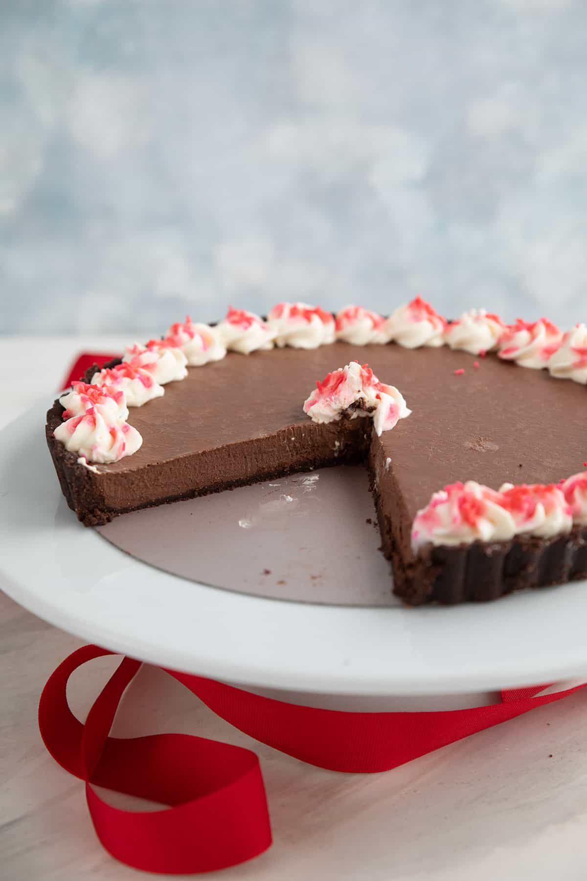 Keto Chocolate Peppermint Tart on a white cake stand with a red ribbon underneath.
