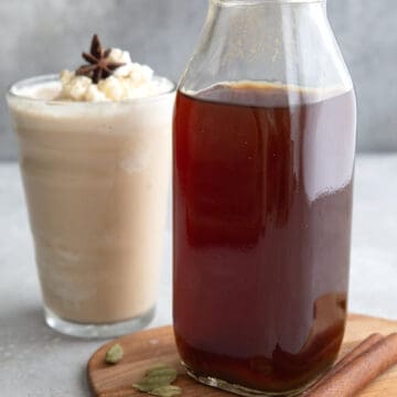 A bottle of Sugar Free Chai Concentrate on a wooden cutting board with a chai Frappuccino in the background.