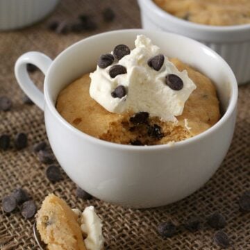 A keto mug cake in a white mug with chocolate chips strewn around and a spoonful taken out of it.
