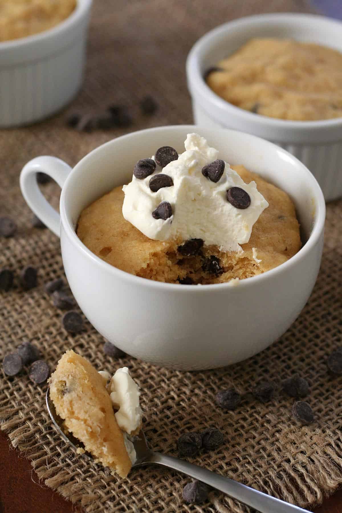 A keto mug cake in a white mug with chocolate chips strewn around and a spoonful taken out of it.