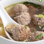 Titled image of a white spoon digging into a bowl of Keto Wonton Meatball Soup.