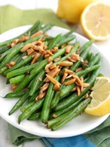 Green Beans Amandine on a white plate with lemons the background.