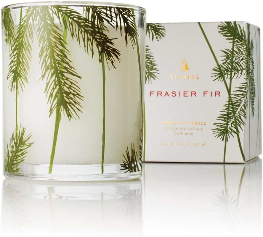 A Frasier Fir candle in a glass candle holder with sprigs of pine on it.