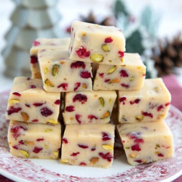 Keto White Chocolate Fudge with cranberries and pistachios piled up on a red patterned plate.
