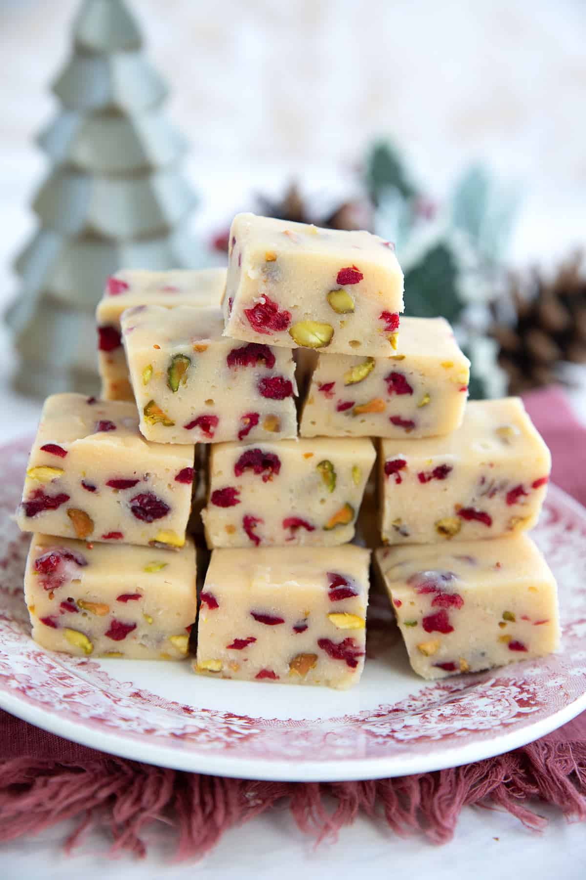 Keto White Chocolate Fudge with cranberries and pistachios piled up on a red patterned plate.