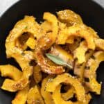 Titled image, top down of a black bowl filled with Parmesan Roasted Delicate Squash, with a sage leaf on top.