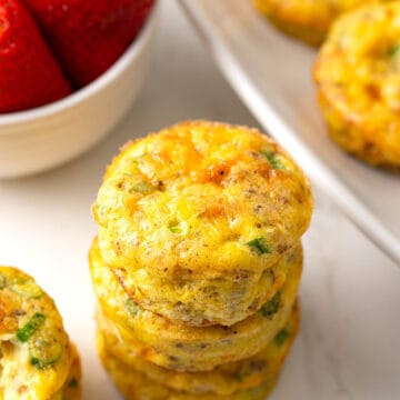 A stack of eggs muffins on a marble tabletop with strawberries in the background.